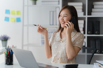 Smiling Businesswoman Phone Call: A young, smiling businesswoman sits at her desk, happily engaged...