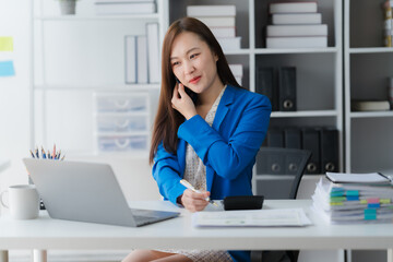 Fototapeta premium Focused Professional: A focused business professional is engrossed in a task, seated at a desk with a laptop and notepad, while maintaining direct eye contact and a thoughtful expression.