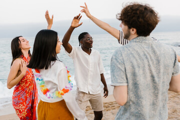 Happy young friends enjoying summer vacation dancing at beach party. Friendship and leisure concept