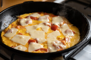 scrambled eggs with tomatoes and pieces of hard cheese in a frying pan on a gas stove