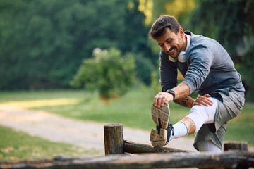 Happy sportsman doing stretching exercises while working out in park.