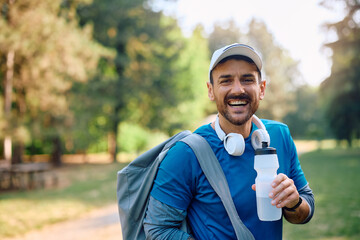 Happy athletic man having water break in park and looking at camera.