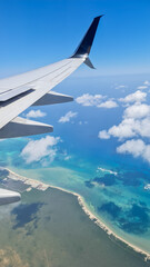 A stunning aerial view from an airplane window, showing the rich blue ocean, lush islands and white clouds floating in the sky, creating a relaxing and serene travel scene.