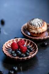 A sweet dessert on the table featuring fresh raspberries, blueberries, and a cheesecake muffin on vintage plates 