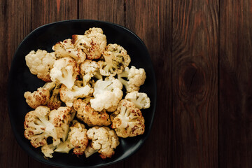 Roasted cauliflower served in a black bowl on a rustic wooden table