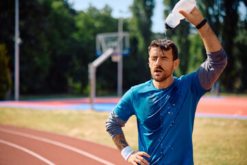 Athletic man pouring water onto his head after sports training outdoors.