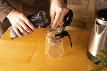 female hands pouring loose leaf tea from a bag into a glass teapot