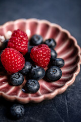Blueberries and raspberries close up on a pink vintage porcelain plate