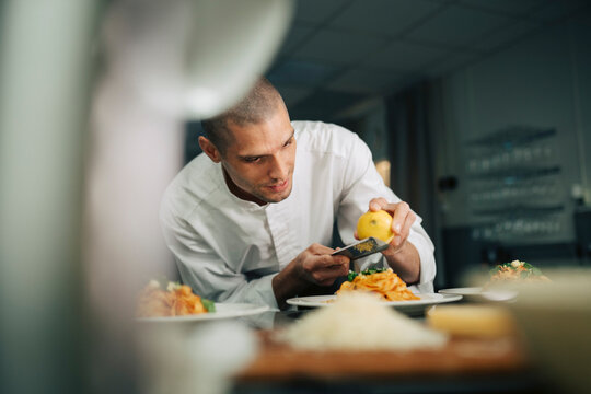 Male chef grating lemon zest on tagliatelle pasta at restaurant kitchen