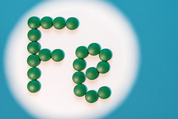 Ferrum, Fe symbol made from pills. Green pills of iron on white background with blue shadows. Healthcare concept