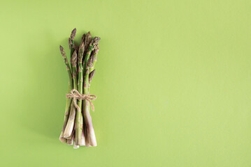 Fresh asparagus tied bundle on vibrant green background. Top view