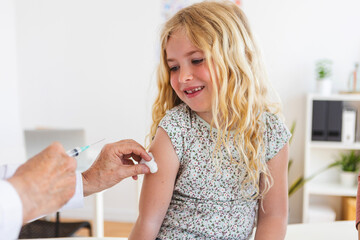 Senior male doctor making vaccination to little girl at hospital room. Children healthcare concept.