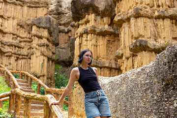 Young woman dressed in black tank top and denim shorts stands gracefully near unique rock...