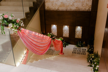 Elegant stairway decor with pink draping and floral arrangements.