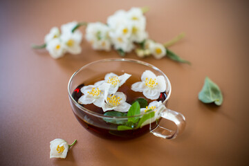 Glass teapot with jasmine and green tea isolated on a brown background