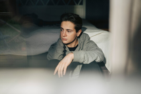 Thoughtful young man looking away while sitting near bed at home