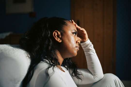 Stressed woman sitting with hand on head near bed in home