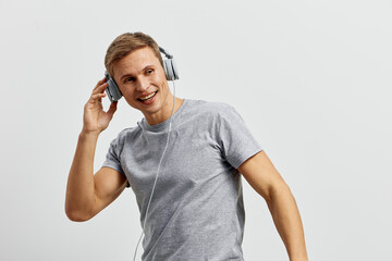Smiling young man wearing casual gray t-shirt listening to music with headphones, looking happy,...
