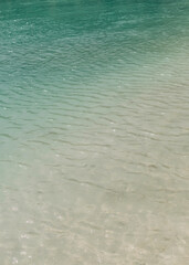 Calm turquoise water gently laps on a sandy shore in a tropical beach setting during midday sunlight