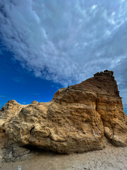Dramatic yellow rock formation on a beach in Odesa, Ukraine, under a dynamic cloudy sky. The textured sandstone contrasts with the deep blue horizon, creating a powerful natural landscape. A scenic
