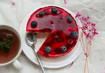 Top view of a delicious berry jelly cheesecake with blueberries and raspberries on a white plate,...