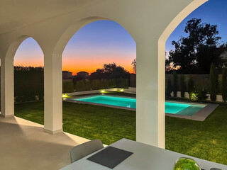 Modern architectural design featuring a serene outdoor pool area at dusk, framed by elegant arches and lush greenery, creating a tranquil evening atmosphere
