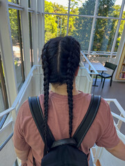 Young woman with braided hair wearing a casual pink shirt and black backpack is walking down a...