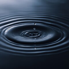 A close-up of a water droplet falling into a calm, dark blue surface, creating ripples and concentric waves.