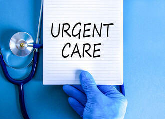 Urgent care symbol. Concept words Urgent care on beautiful white note. Doctor's hand in blue medical glove. Stethoscope. Beautiful blue background. Medical healthy lifestyle urgent care concept.
