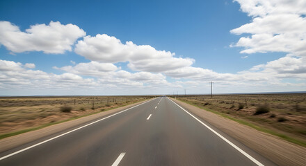 Fototapeta premium A long, straight highway stretches across a vast, flat landscape under a bright, partly cloudy sky.