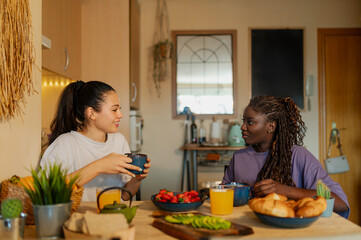 Two women are sharing a healthy and delicious breakfast in their cozy kitchen, enjoying each...