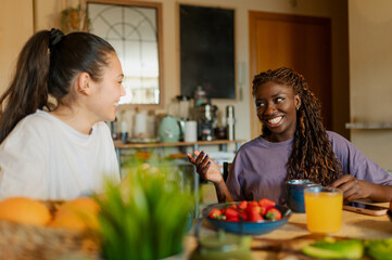 Two women enjoying a healthy breakfast at home, sharing smiles and laughter while engaging in...