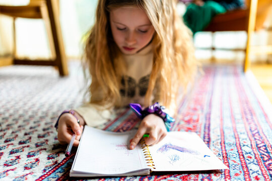 Girl learning spellings from book while lying down on carpet at home