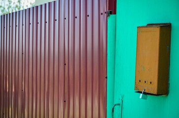 A brown box with a lock on it is next to a green wall. The box is on the side of a building