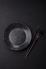 Empty round black plate for food, kitchen utensils on dining table. Empty plate