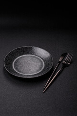 Empty round black plate for food, kitchen utensils on dining table. Empty plate