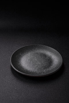 Empty round black plate for food, kitchen utensils on dining table. Empty plate
