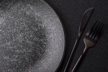 Empty round black plate for food, kitchen utensils on dining table. Empty plate