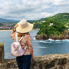 Tourist woman with hat from behind and enjoying the views of La Concha Bay, San Sebastian, Basque Country