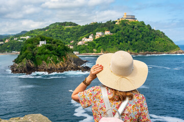 Tourist woman with hat from behind and enjoying the views of La Concha Bay, San Sebastian, Basque Country