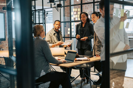 Team of excited business professionals discussing with entrepreneur in meeting room at office