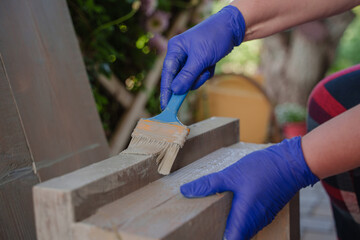 A woman paints a wooden product gray with a brush.