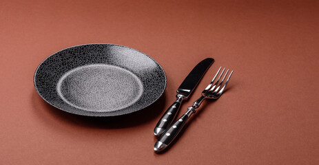 Empty round black plate for food, kitchen utensils on dining table. Empty plate