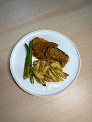 A plate of pork belly with potato and asparagus.