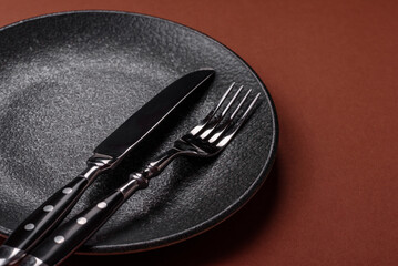 Empty round black plate for food, kitchen utensils on dining table. Empty plate