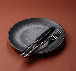 Empty round black plate for food, kitchen utensils on dining table. Empty plate