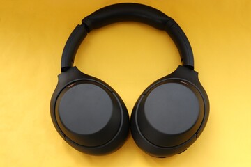 modern black wireless headphones on a yellow background as a symbol of mobility and technological...