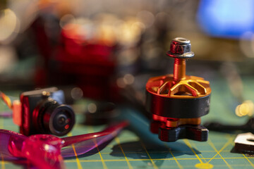 FPV drone motor and components on workbench with focus on vibrant orange and red parts