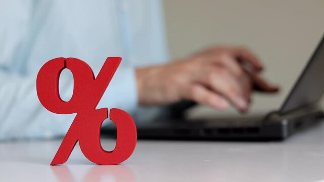 Red sign of percent on the table. Man using laptop on the background