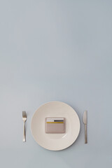 Card wallet lies on plate surrounded by fork and knife. Vertical banner for food expenses concept....